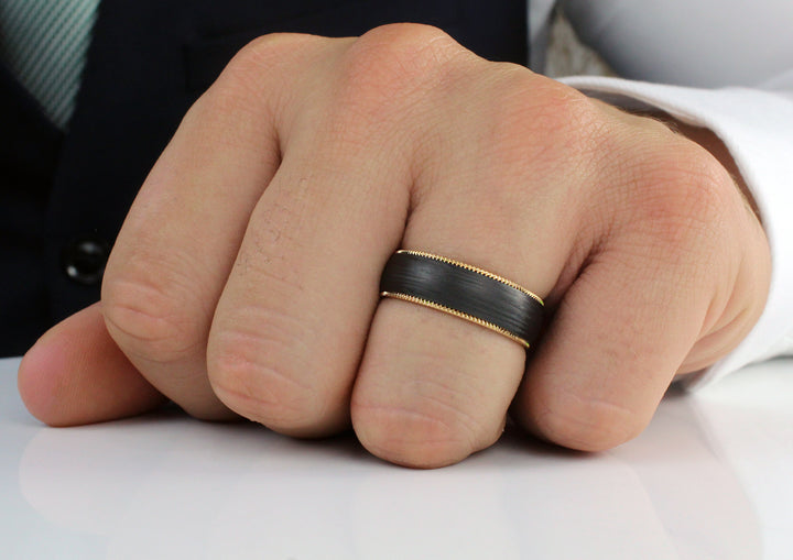 Model wearing Pair of 6.5mm wide 18ct yellow gold & Black Carbon Fibre ring; traditional court shaped profile with milgrain edging detail.